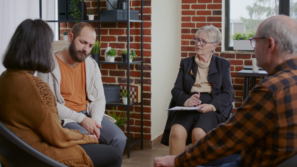 Elderly people participating in a grief support group with a therapist in a warm and compassionate counselling setting.