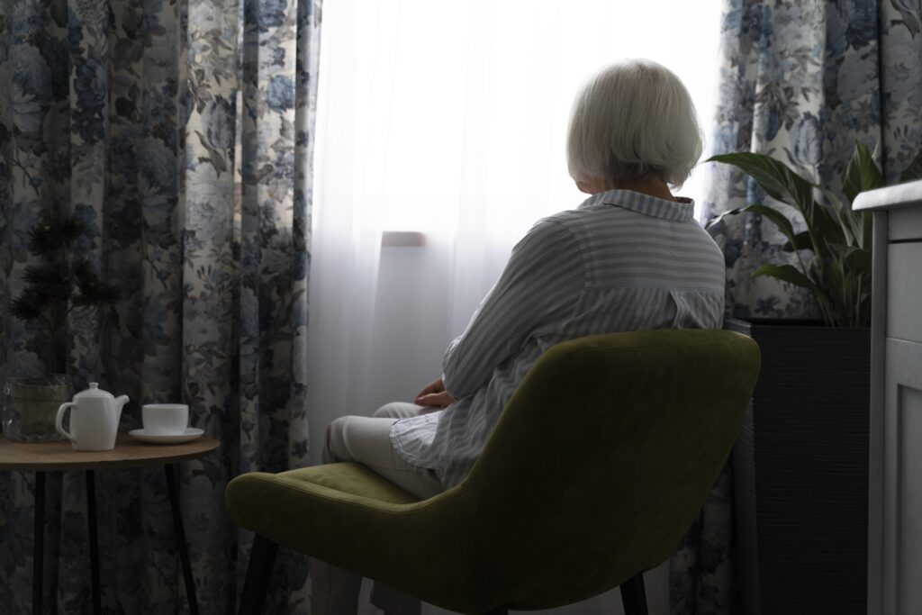 Older adult sitting thoughtfully by a window, reflecting the often unnoticed emotional signs of depression in later life.