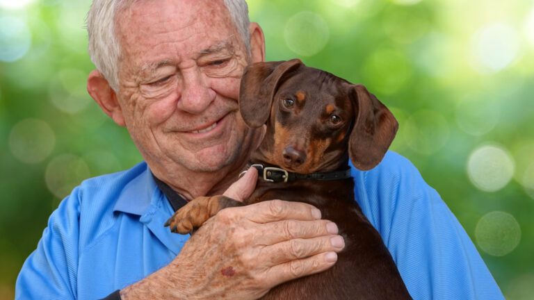 Senior adult smiling while holding a pet dog at home, highlighting the psychological benefits of pet companionship in later life.